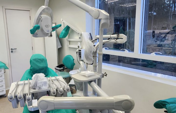 Equipamento odontológico em detalhe, junto à janela com vista das árvores